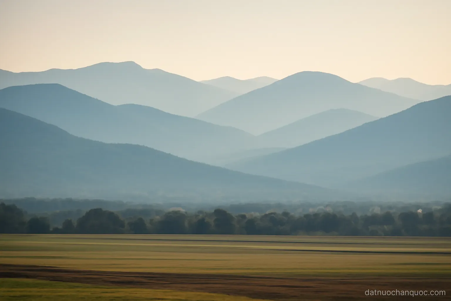 layered mountain ridges fading into haze with a narrow strip of flat farmland in front
